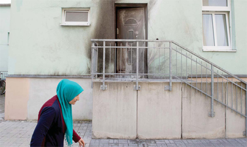 DRESDEN, Germany: A woman wearing a headscarf walks past the entrance to the Fatih Camii Mosque, where traces of smoke can be seen after a bomb attack. — AFP