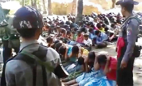 MYANMAR: This screen grab taken yesterday from a YouTube video originally taken by Myanmar Constable Zaw Myo Htike shows policemen standing guard around Rohingya minority villagers seated on the ground in the village of Kotankauk during a police area clearance operation. — AFP