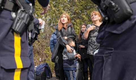 An extended family of 8 people from Colombia are detained by Royal Canadian Mounted Police officers after they illegally crossed the border near Hemmingford, Quebec. — AFP