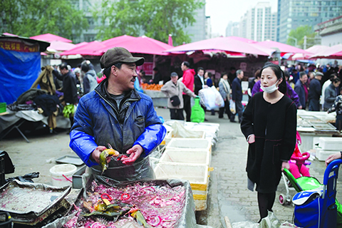 A vendor prepares fresh fish for a customer (R) at a market in Beijing on April 7, 2017. / AFP / NICOLAS ASFOURI