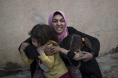 A woman holds her daughters as gunshots are heard in a neighborhood recently liberated by Iraqi security forces in western Mosul, Iraq. - AP