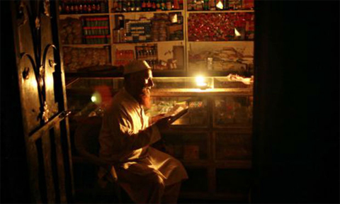  A store owner reads by candlelight during a power cut in Islamabad. (Photo: AP)