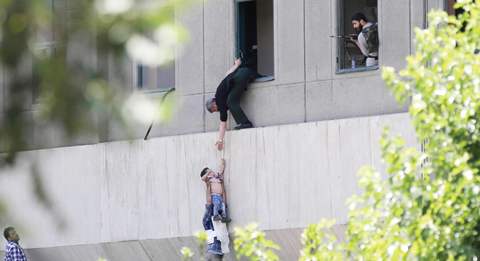 TEHRAN: Iranian policemen evacuate a child from the parliament building in Tehran yesterday during an attack on the complex. - AFP 