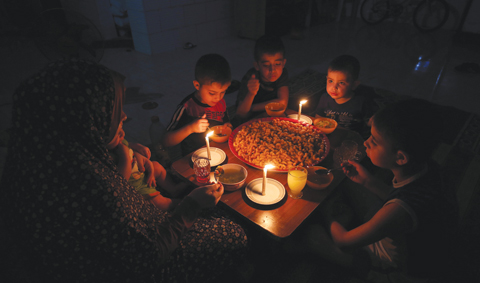 GAZA: A Palestinian family eats dinner by candlelight at their makeshift home in the Rafah refugee camp in the southern Gaza Strip during a power outage on Sunday. — AFP