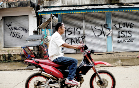 MARAWI, Philippines: A man rides his motorcycle past shuttered shop fronts sprayed with pro- Islamic State group graffiti yesterday. —AFP