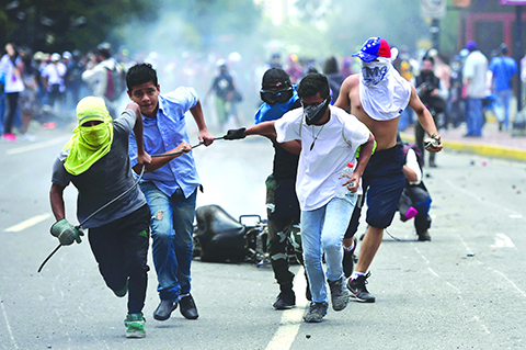 CARACAS: Anti-government activists drag a police motorbike burnt after the explosion of an explosive device during a protest against the elections for a Constituent Assembly. - AFP 