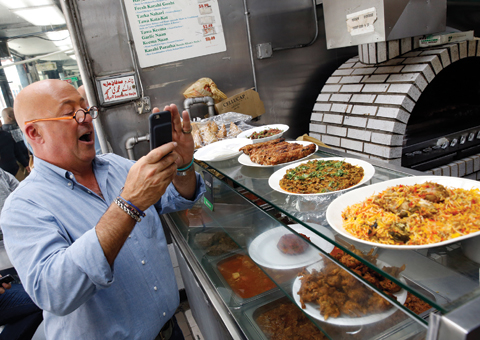 Andrew Zimmern snaps a cell phone photo of chicken kebabs, far left, a dish composed of organ meats, center, and a goat dish called katakat at Kababish. — AP photos
