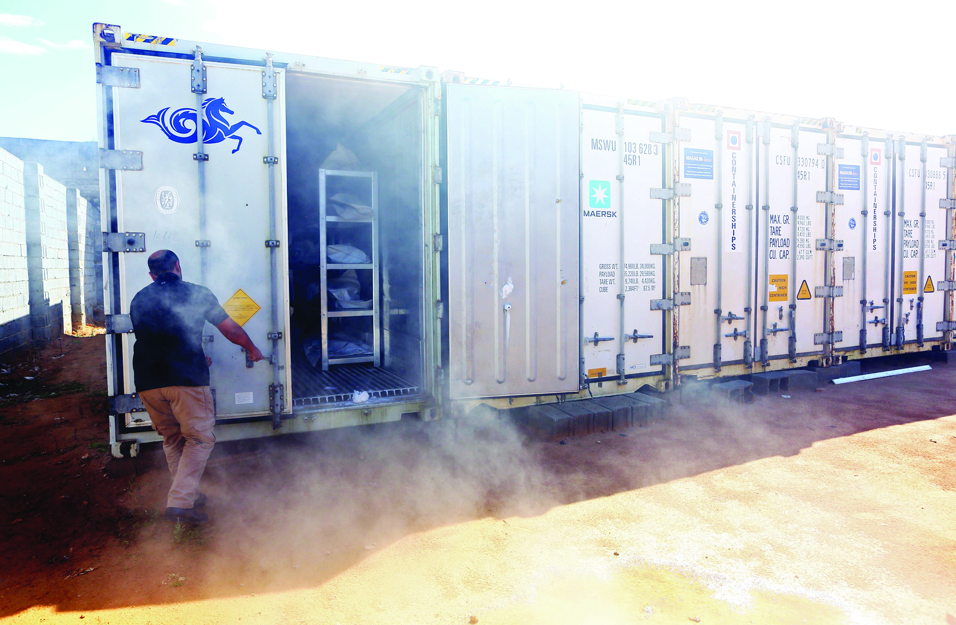 MISRATA: Ali Tuwaileb who is in charge of a high security anti-organized crime complex in Misrata where the bodies of Islamic State (IS) group fighters are being stored opens one of the refrigerated containers at a make-shift morgue. - AFP 