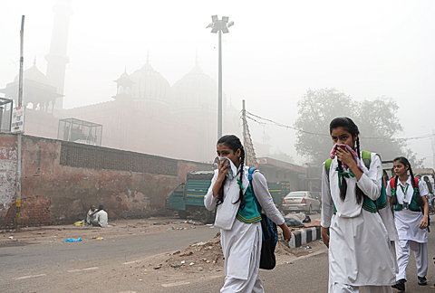 NEW DELHI: Indian schoolchildren cover their faces as they walk to school amid heavy smog in New Delhi yesterday. —AFP