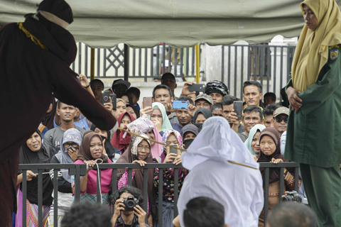 BANDA ACEH: People watch as Tjia Nyuk Hwa, 45, an Indonesian Christian, is publicly flogged outside a mosque in Banda Aceh yesterday, for playing a children’s entertainment game seen as violating Islamic law. — AFP photos