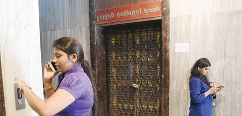 MUMBAI: A woman speaks on her phone while a journalist waits next to the sealed entrance of the Brady House branch of the Punjab National Bank (PNB) which had been sealed in Mumbai yesterday.—AFP