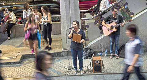 A blind singer performing in front of a skytrain station in Bangkok. — AFP photos