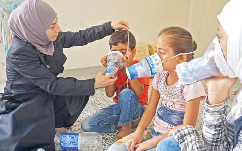 BINNISH, Syria: Um Majid tries an improvised gas mask on family members in her home in Syria's rebel-held northern Idlib province as part of preparations for any upcoming raids yesterday. - AFP 