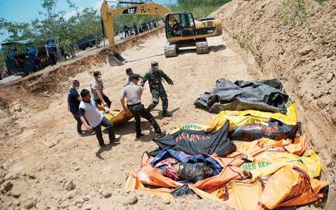 PALU, Indonesia: Officials carry body bags into a mass grave ahead of a mass funeral for quake victims in Palu, in Central Sulawesi yesterday. — AFP