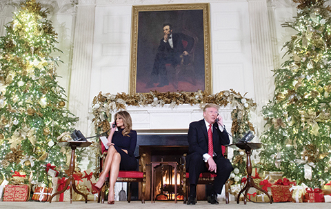 TOPSHOT - US President Donald Trump and First Lady Melania Trump speak on the telephone as they answers calls from people calling into the NORAD Santa tracker phone line in the State Dining Room of the White House in Washington, DC, on December 24, 2018. (Photo by SAUL LOEB / AFP)