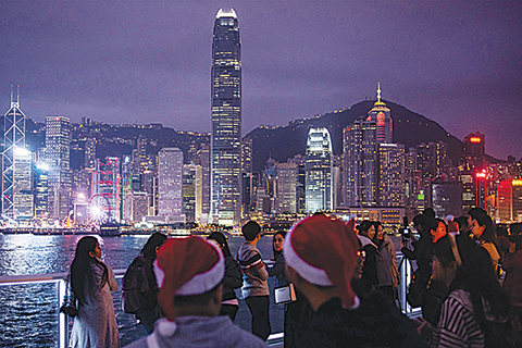 People clad in Santa hats (foreground) look on as the city skyline is seen along Hong Kong's Victoria Harbour on December 25, 2018. (Photo by Philip FONG / AFP)