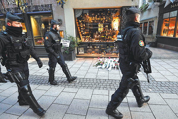 nSTRASBOURG: French gendarmes walk past flowers and candles laid in the street in tribute to the victims of a deadly shooting two days ago, in central Strasbourg.-AFP 