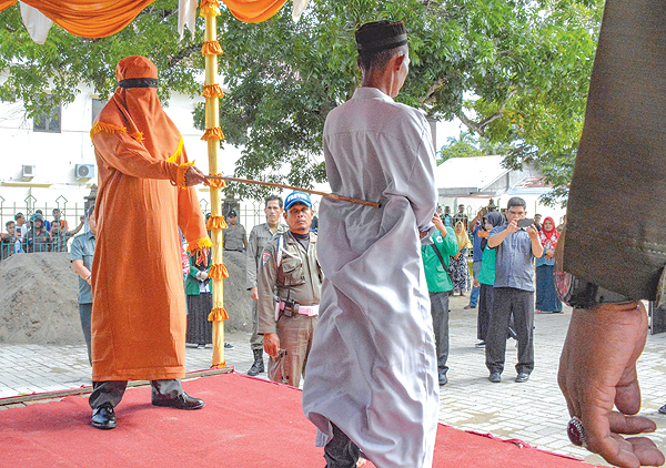 EAST ACEH: A Sharia law enforcement official whips a man in East Aceh, in Aceh province yesterday. A group of men were publicly whipped for breaking Islamic law in Indonesia’s Aceh in front of a jeering crowd for being involved in online gambling. — AFP