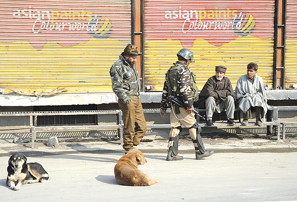 KASHMIR: Kashmiri Muslim men sit in front of closed shops as Indian paramilitary troopers patrol during the second day of three days strike called by Kashmiri separatists in Srinagar. — AFP