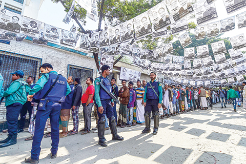 TOPSHOT - Bangladeshi voters wait in line outside a polling station while security police officials watch over in Dhaka on December 30, 2018. - Bangladesh headed to the polls on December 30 following a weeks-long campaign that was dominated by deadly violence and allegations of a crackdown on thousands of opposition activists. (Photo by Munir UZ ZAMAN / AFP)