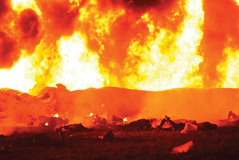 TLAHUELILPAN, Mexico: A fire rages behind the bodies of burned victims at the scene of a massive blaze triggered by a leaky pipeline early yesterday. - AFP  