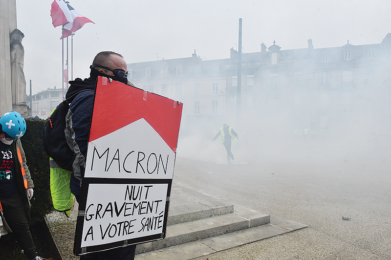 LE MANS: A protester carries a placard depicting a cigarette pack and reading “Macron seriously harms health” as he stands in tear gas smoke during an anti-government demonstration called by the “Yellow Vest” (Gilets Jaunes) movement. — AFP