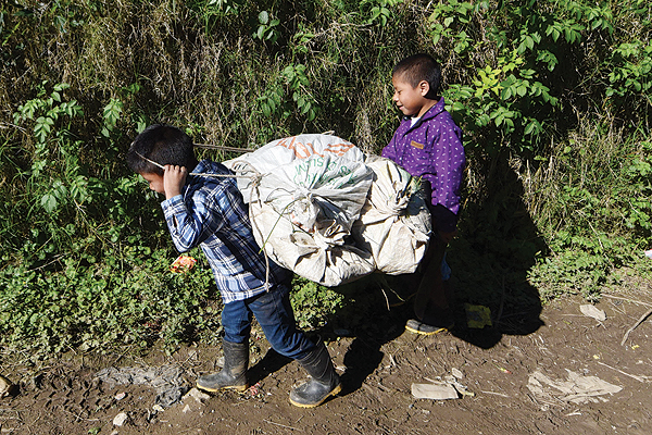 GUATEMALA: A couple of children carry sacks along a dirt path in Yalambojoch, home village of eightyear- old migrant Felipe Gomez, who died in a medical center in Alamogordo, New Mexico.—AFP