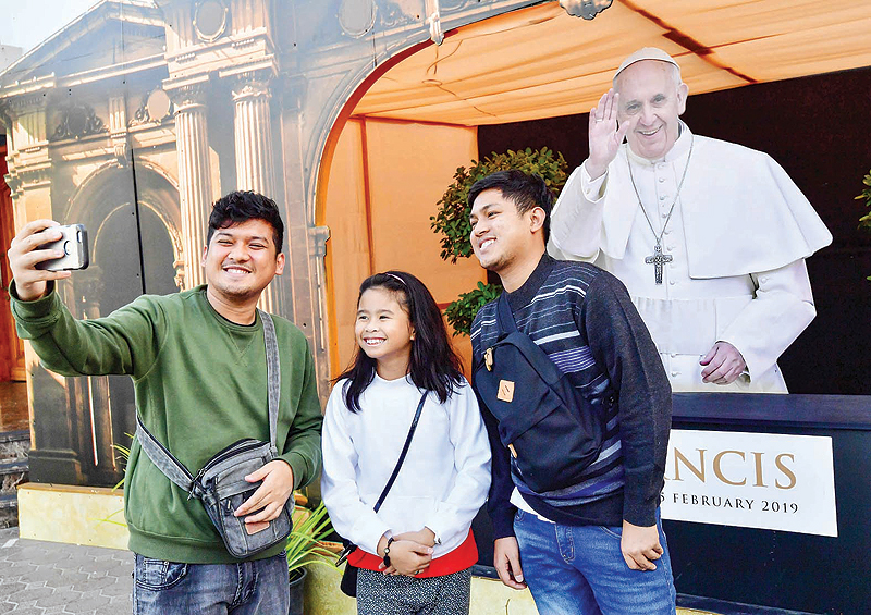 DUBAI: Two men and a girl pose for a selfie with a cutout image of Pope Francis, days ahead of his visit to the United Arab Emirates, at St Mary’s Catholic Church on Wednesday. — AFP