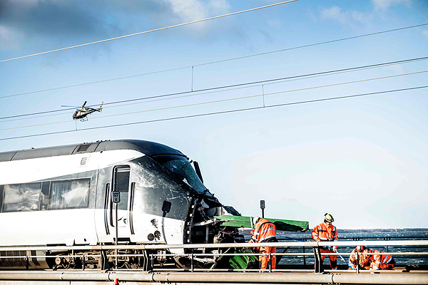 NYBORG, Denmark: Men work at the accident site next to a passenger train standing on the rails after a railway accident yesterday. — AFP
