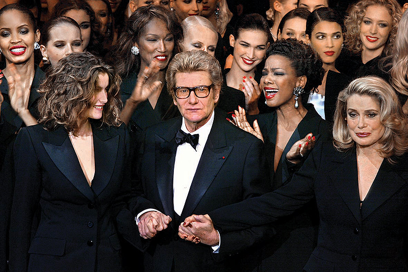 In this file photo taken on January 22, 2002 French fashion designer Yves Saint- Laurent (center) salutes the crowd with French model Laetitia Casta (left) and French actress Catherine Deneuve (right) at the Centre Georges Pompidou national museum for modern art in Paris, during Saint-Laurentís last fashion show