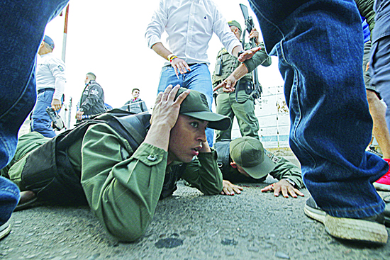 TOPSHOT - Two Venezuelan soldiers lie on the ground as they are detained by Colombian police after driving into Colombia in an armor car from the Venezuelan side of Simon Bolivar International bridge in Cucuta on February 23, 2019. - According to Colombian authorities four soldiers of the Venezuelan guard deserted this Saturday after crossing two border bridges with Colombia, closed by order of the government of Nicol·s Maduro before the announcement of the entry of aid shipments. Three of the soldiers were mobilized in a white tank and knocked down one of the security fences of the SimÛn BolÌvar Bridge, in the Colombian city of C˙cuta, said a Colombian Immigration officer (Photo by Schneyder Mendoza / AFP)
