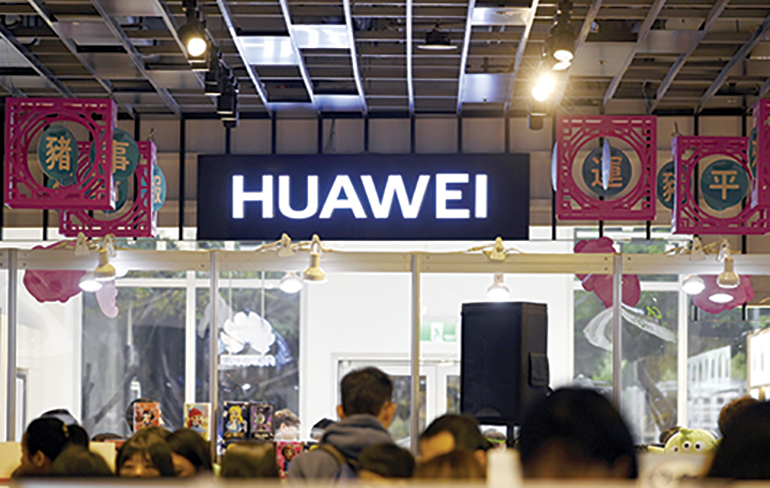 People stand near a logo of Chinese telecoms giant Huawei at the Syntrend Creative Park in Taipei on February 9, 2019. (Photo by SAM YEH / AFP)