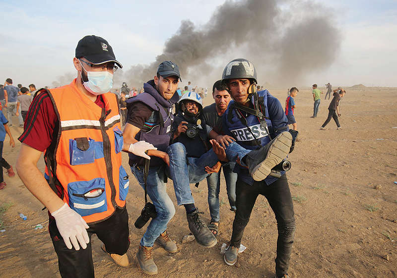 GAZA: In this file photo, Palestinian paramedics and journalists carry a wounded fellow journalist during clashes with Israeli forces east of Gaza city, along the Gaza-Israel border. — AFP