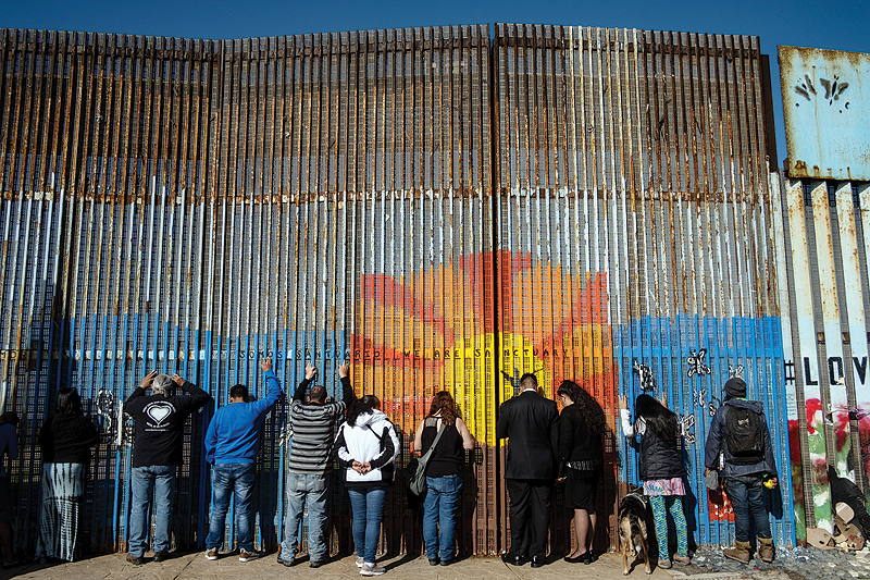 People pray as they lean against the US-Mexico border fence, during the celebration of a religious service on both sides of the fence in Playas de Tijuana, Baja California state, Mexico. — AFP