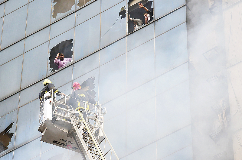 DHAKA: People trapped inside a burning office building gesture at Bangladeshi firefighters for help in Dhaka yesterday. A huge fire tore through a Dhaka office block, killing at least five people with many others feared trapped in the latest major inferno to hit the Bangladesh capital. — AFP