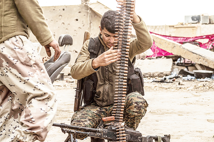 A fighter of the US-backed Syrian Democratic Forces (SDF) loads an ammunition belt at a position in the village of Baghouz, near Syria's border with Iraq, in the eastern Deir Ezzor province on March 15, 2019 during the SDF's preparations to advance in the battle against the last pocket of Islamic State group (IS) jihadists. (Photo by Delil SOULEIMAN / AFP)