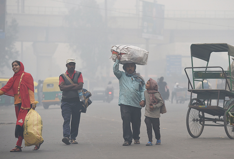NEW DELHI: A family carries belongings while looking for a rickshaw amid heavy smog in New Delhi. For the well-heeled in New Delhi, eating out means enjoying a gourmet spread amid sprawling green spaces but the poor must deal with dust and toxic fumes from vehicles zipping past rickety roadside food stalls in the world's most polluted major city. - AFP n