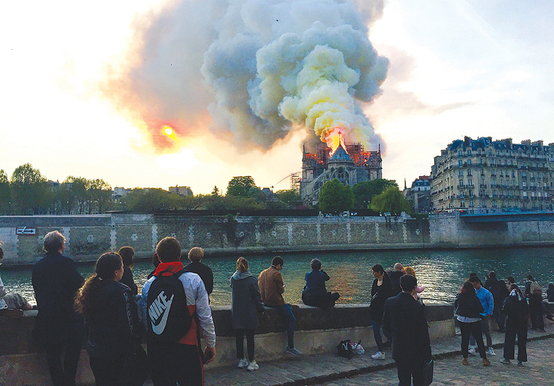 PARIS: Bystanders look on as flames and smoke billow from the roof at Notre-Dame Cathedral in Paris. — AFP