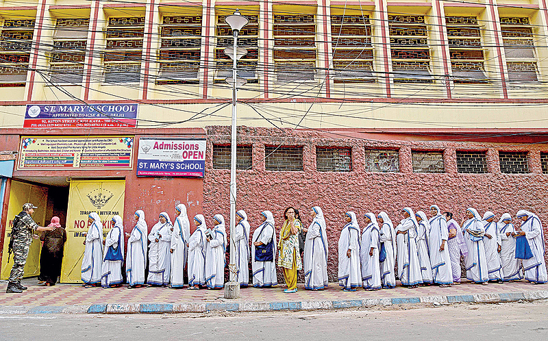 Indian nuns from the Mother Teresa Missionaries of Charities queue to cast their votes as a paramilitary force personnel stands guard at a polling station at St Mary’s School in Kolkata yesterday. (Inset) Indian voters pose for a picture as they show their ink-marked finger after casting their vote at a polling center on the outskirts of Amritsar yesterday. —AFP