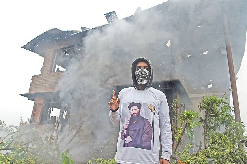 TRAL: A Kashmiri protester wears a shirt depicting a picture of militant commander Zakir Musa stands in front of a damaged house following a gun battle in Dadsar village south of Srinagar on Friday. — AFP