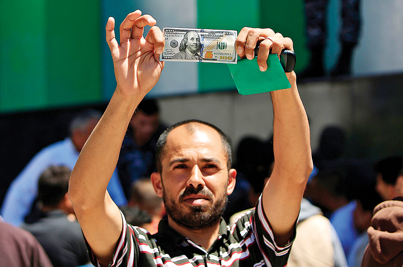 GAZA: A Palestinian man displays a 100 dollar bill, part of $480 million in aid allocated by Qatar, in Gaza City yesterday. - AFP 