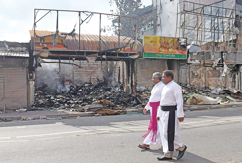 MINUWANGODA, Sri Lanka: Sri Lankan Catholic priests walk past a damaged shop after a mob attack yesterday. — AFP