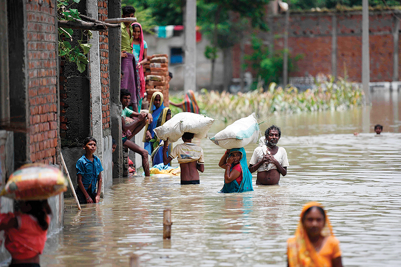 BIHAR: Indian residents wade along a flooded street carrying their belongings following heavy monsoon rains at Sitamarhi district in the Indian state of Bihar. — AFP