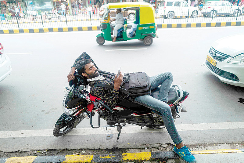NEW DELHI: A man uses a mobile phone leaning on a motorbike along a street in New Delhi yesterday. — AFP
