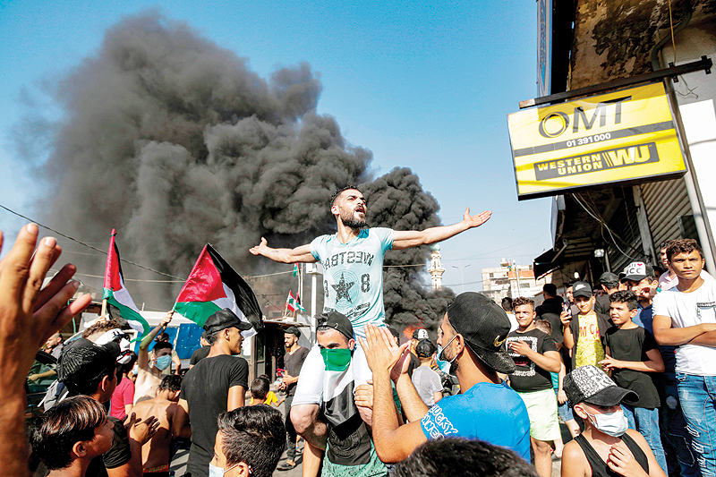 BEIRUT: A man chants slogans while lifted on the shoulders of another wearing a Palestinian flag as a bandanna, as protesters block the main road outside the Palestinian refugee camp of Burj Al-Barajneh south of the Lebanese capital yesterday. - AFP  