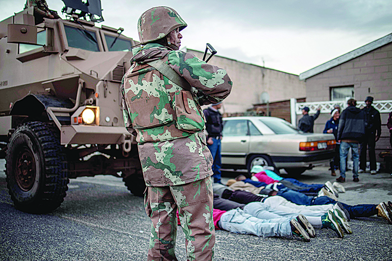 A South African National Defence Forces soldier stands guard as suspects lay on the ground after being searched for drugs and weapons during a joint police operation in the Mitchel's Plan district of the Cape Flat in Cape Town, on August 9, 2019. - A total of 1320 South Africa National Defence Forces service members have been deployed to Cape Town's gang-ridden areas to support police operations to prevent and combat crime. (Photo by MARCO LONGARI / AFP)