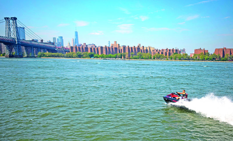 A man steers his Jet sky in the East River in front of the Williamsburg bridge on August 19, 2019 in New York City. - Northern hemisphere summers will deliver dangerously longer heatwaves, droughts and bouts of rain even if humanity manages to cap global warming at two degrees Celsius, scientists said. (Photo by Johannes EISELE / AFP)
