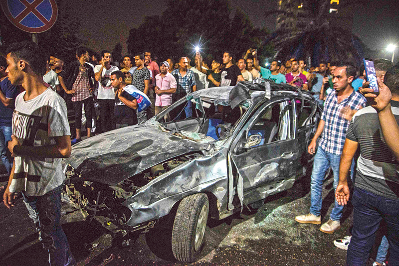 CAIRO: Onlookers gather around a charred car just before midnight on Sunday outside the National Cancer Institute in the Egyptian capital. - AFP 