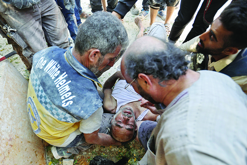 TOPSHOT - Members of the Syrian Civil Defence (White Helmets) carry an injured man after removing him from under the rubble of a building that collapsed during reported air strikes by pro-regime forces in the village of Beinin, north of Maaret al-Numan, in the northern Idlib province, on August 20, 2019. - Jihadists and allied rebels withdrew from Khan Sheikun and the countryside to its south in northwestern Syria in the early hours today as President Bashar al-Assad's forces pressed an offensive against the jihadist-run Idlib region, a war monitor said. (Photo by Omar HAJ KADOUR / AFP)