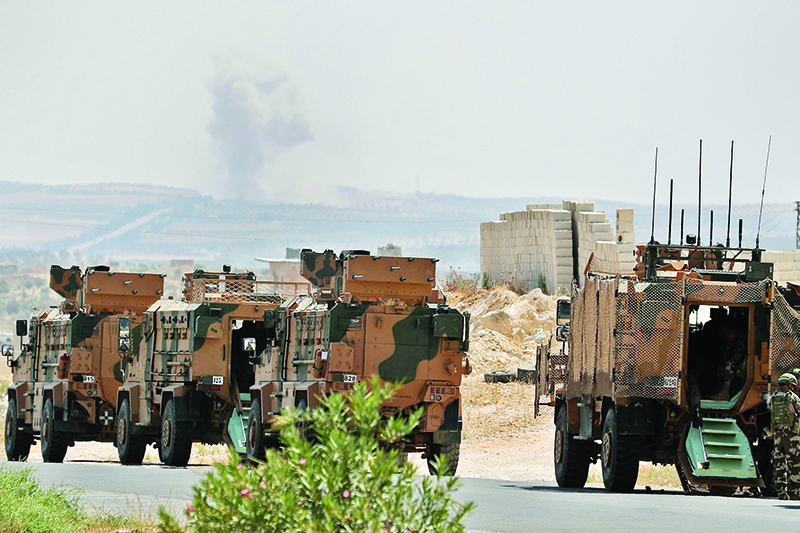 A convoy of Turkish military vehicles is pictured near the town of Maar Hitat as smoke billows in the background, during reported air strikes by pro-regime forces in northern Syria's Idlib province on August 19, 2019. - A Turkish military convoy crossed into northwest Syria today, heading towards a key town where regime forces are waging fierce battles with jihadists and rebels. (Photo by Omar HAJ KADOUR / AFP)